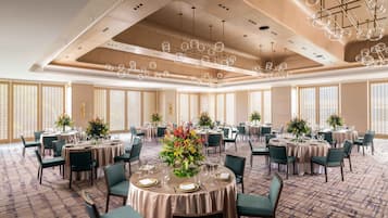 A spacious banquet hall with round tables, green upholstered chairs, and a patterned carpet.