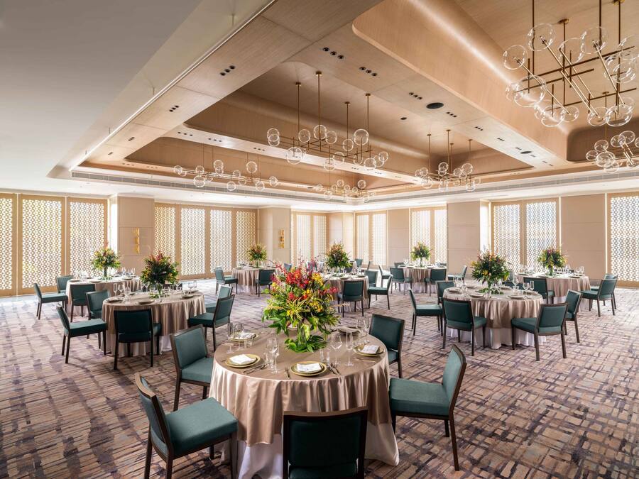 A spacious banquet hall with round tables, green upholstered chairs, and a patterned carpet.