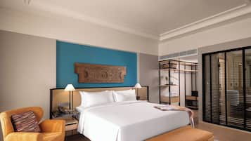 A modern hotel room with a large bed, a desk, a chair, a bench, a wardrobe, and a large window.