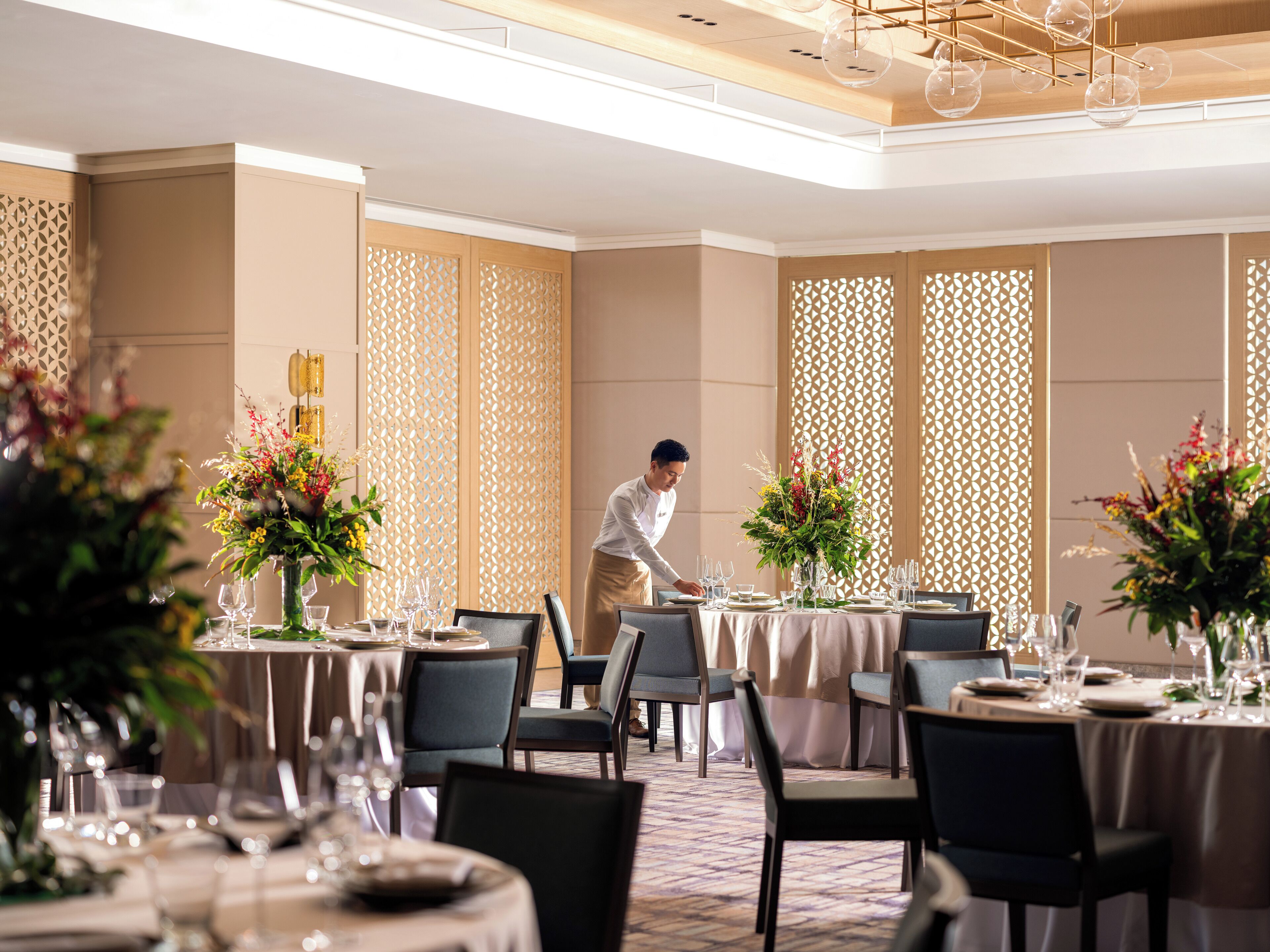 A well-lit dining area with round tables, chairs, and floral centerpieces.