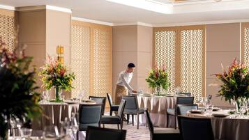 A well-lit dining area with round tables, chairs, and floral centerpieces.