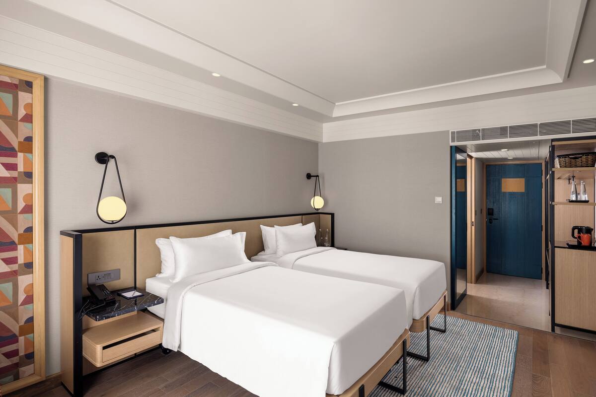 Habitación de hotel con dos camas, un escritorio, un teléfono, una lámpara y un armario.