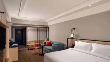 Una habitación de hotel con cama, escritorio, silla, mesita pequeña y lámpara de pared.
