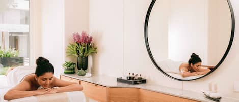 A spa room with a massage table, a large mirror, a wooden vanity, and a potted plant.