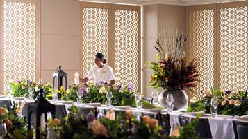 Un espace repas avec des tables dressées pour le service, un serveur et des compositions florales décoratives.