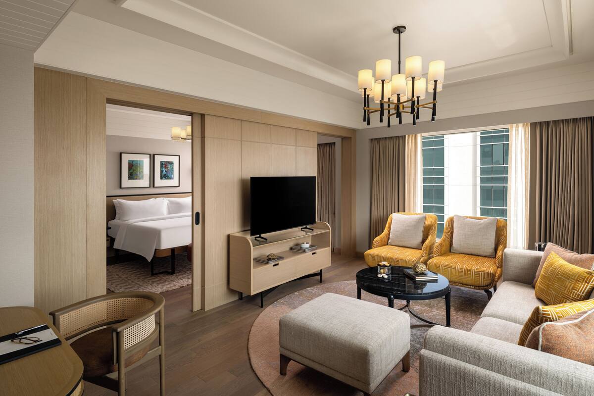 Una habitación de hotel moderna con televisión, sofá, sillón y un área de comedor con mesa y sillas.