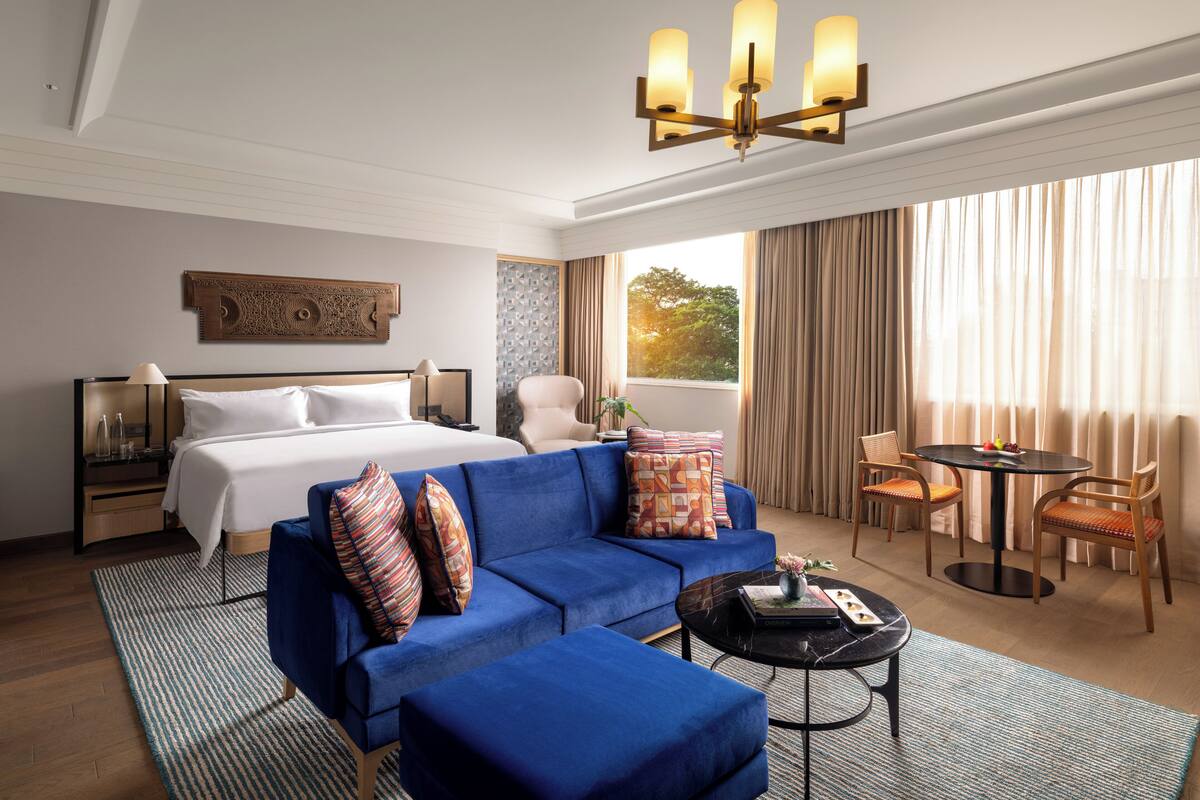 Una habitación de hotel con una cama grande, un sofá azul, una mesita redonda y una araña.