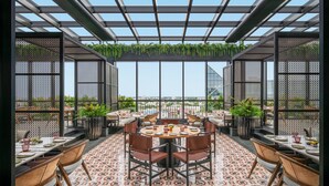 An outdoor dining area with a patterned floor, round tables, and chairs, surrounded by a glass ceiling and metal railings. - Pullman Chennai Anna Salai - Premium Brand By Accor (Chennai)