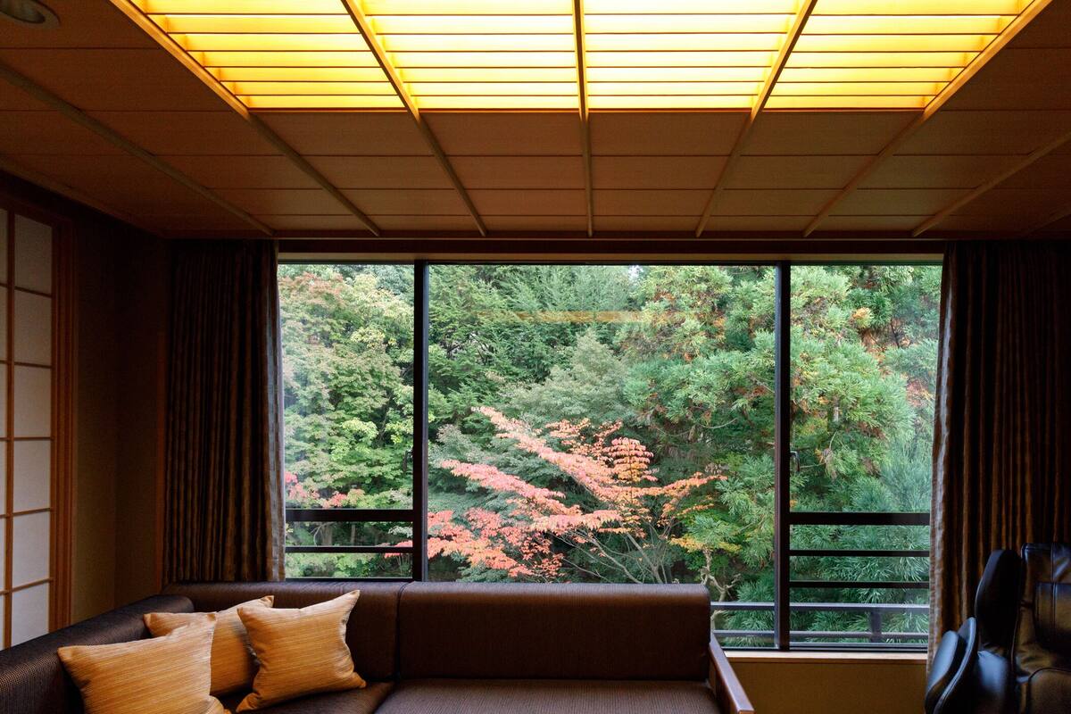 Una habitación moderna con un ventanal grande, un sofá marrón oscuro y una silla de masaje negra.