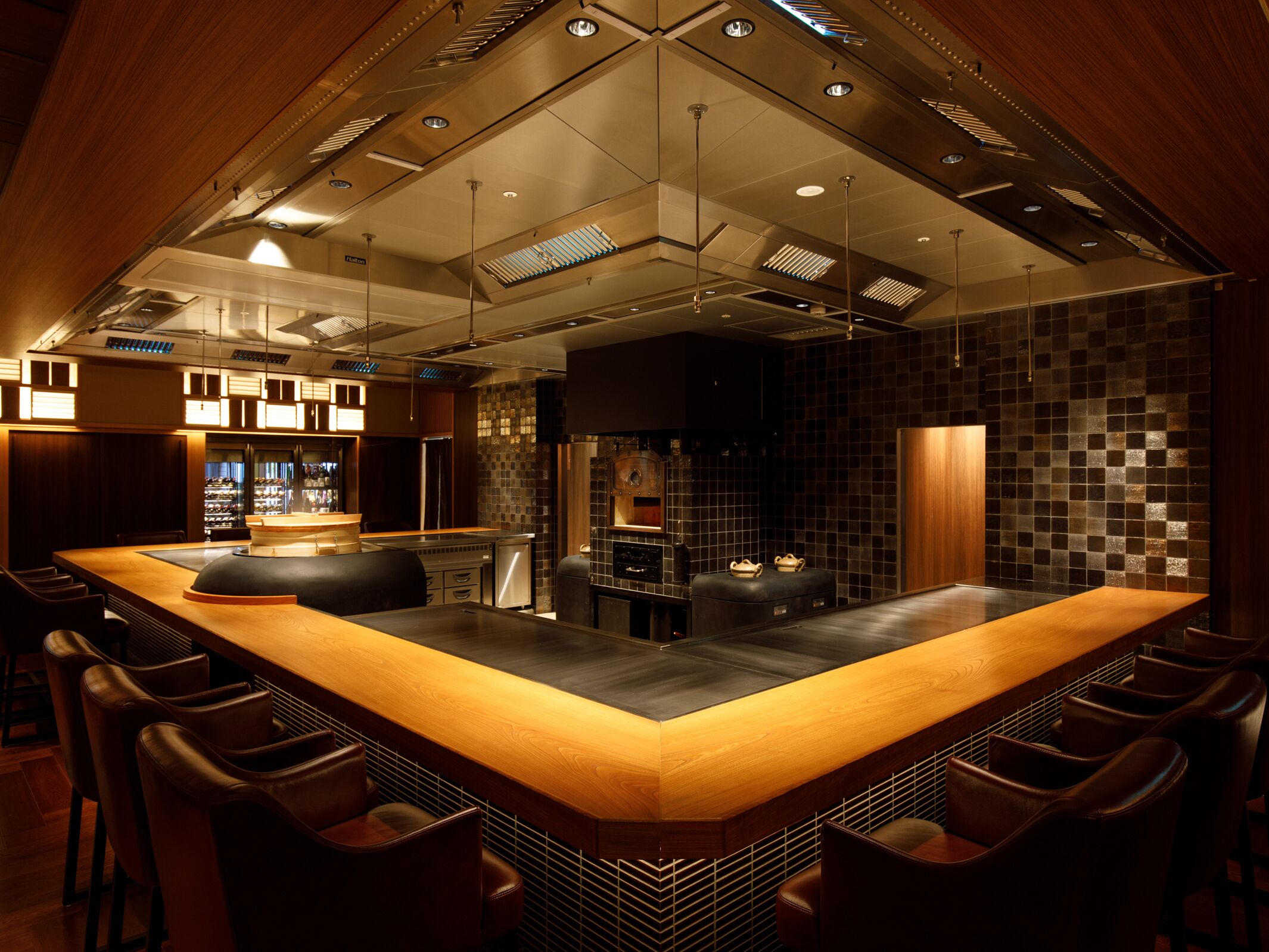 A modern kitchen with a central island, bar stools, and a dark tiled backsplash.