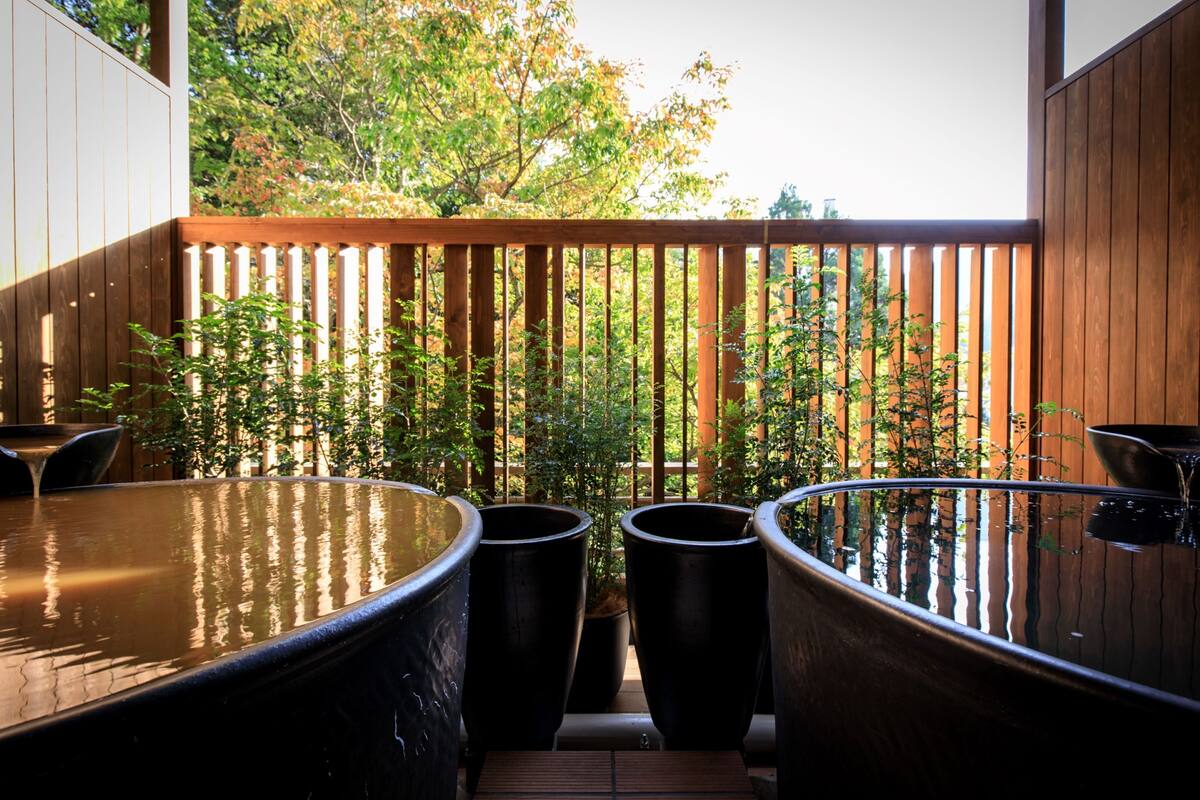 Zona de spa con tinas grandes y una terraza de madera con vistas a un jardín.