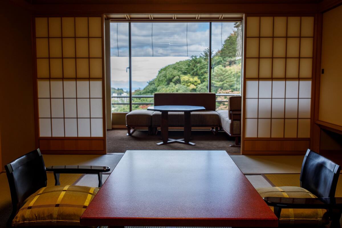 Una habitación japonesa tradicional con suelo de tatami, una mesa baja y vistas a un balcón con barandilla de madera.