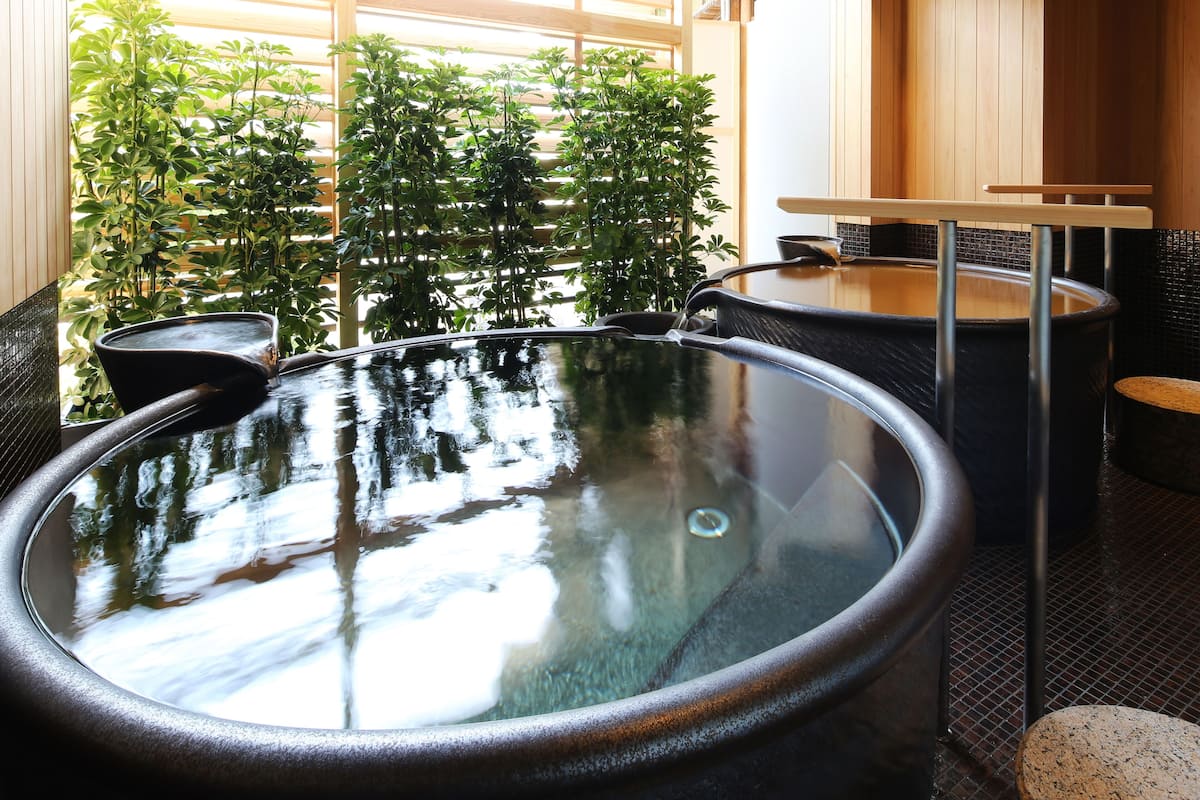 Zona de baños termales con una gran cuenca circular, rodeada de paredes de madera y plantas en macetas.
