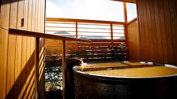 A wooden sauna with a large barrel bath, a window with a view of mountains, and a wooden railing.