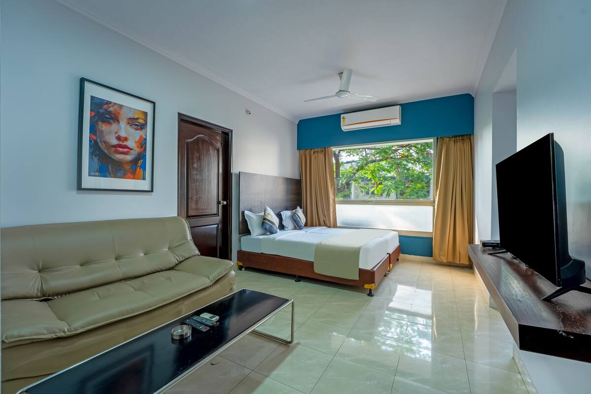 A hotel room with a bed, a sofa, a television, and a painting on the wall.