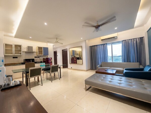 A modern living room with a sofa, a dining area with chairs and a table, a kitchen with cabinets, and a ceiling fan.