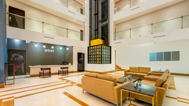 Un hall d’entrée spacieux au design moderne, comprenant un comptoir d’accueil, un espace salon et un escalier menant aux étages supérieurs.