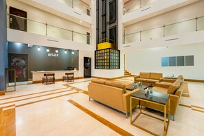 Um hall amplo com design moderno, destacando um balcão de recepção, área de estar e uma escadaria para os andares superiores.