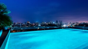 Una piscina en la azotea con vista a la ciudad de noche.