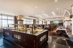 Un'area buffet con diversi cibi, una zona salotto con tavoli e sedie, e un'ampia finestra con tende.