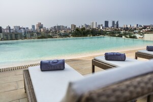 Piscina en la azotea con sillones de descanso y vista al horizonte de la ciudad.