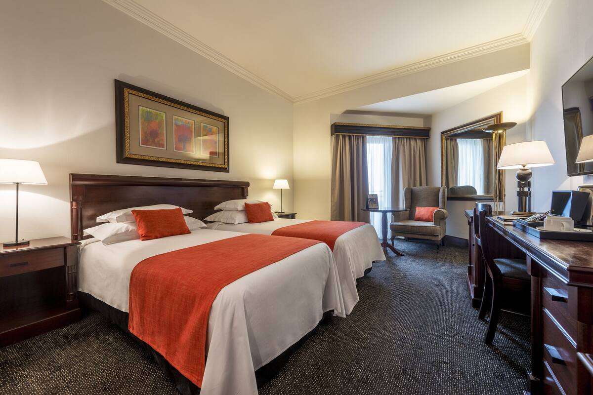 Hotellihuone, jossa on kaksi sänkyä, työpöytä, tuoli ja suuri peili.