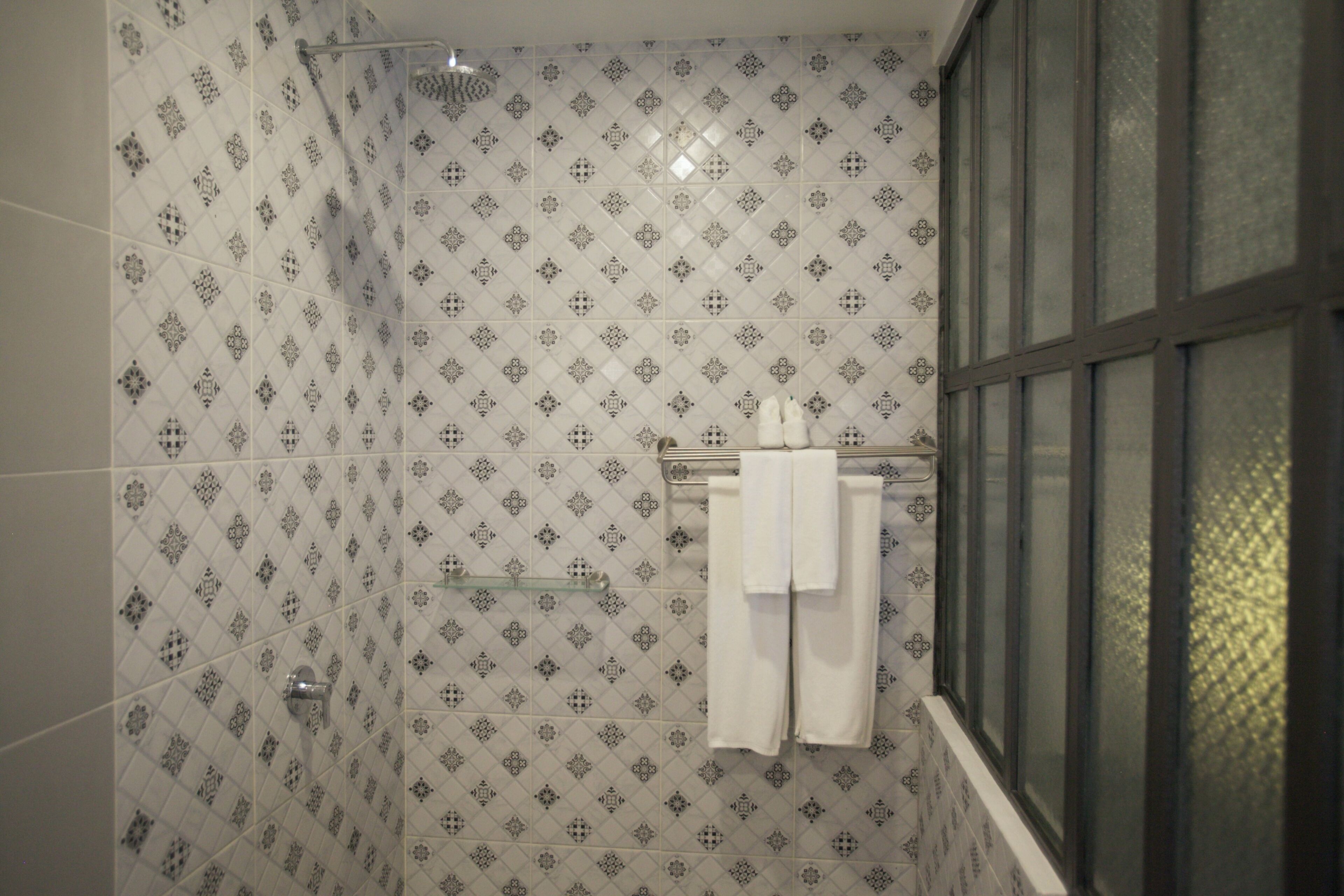 Un baño con baldosas estampadas, cabina de ducha de vidrio y ventana con vistas.