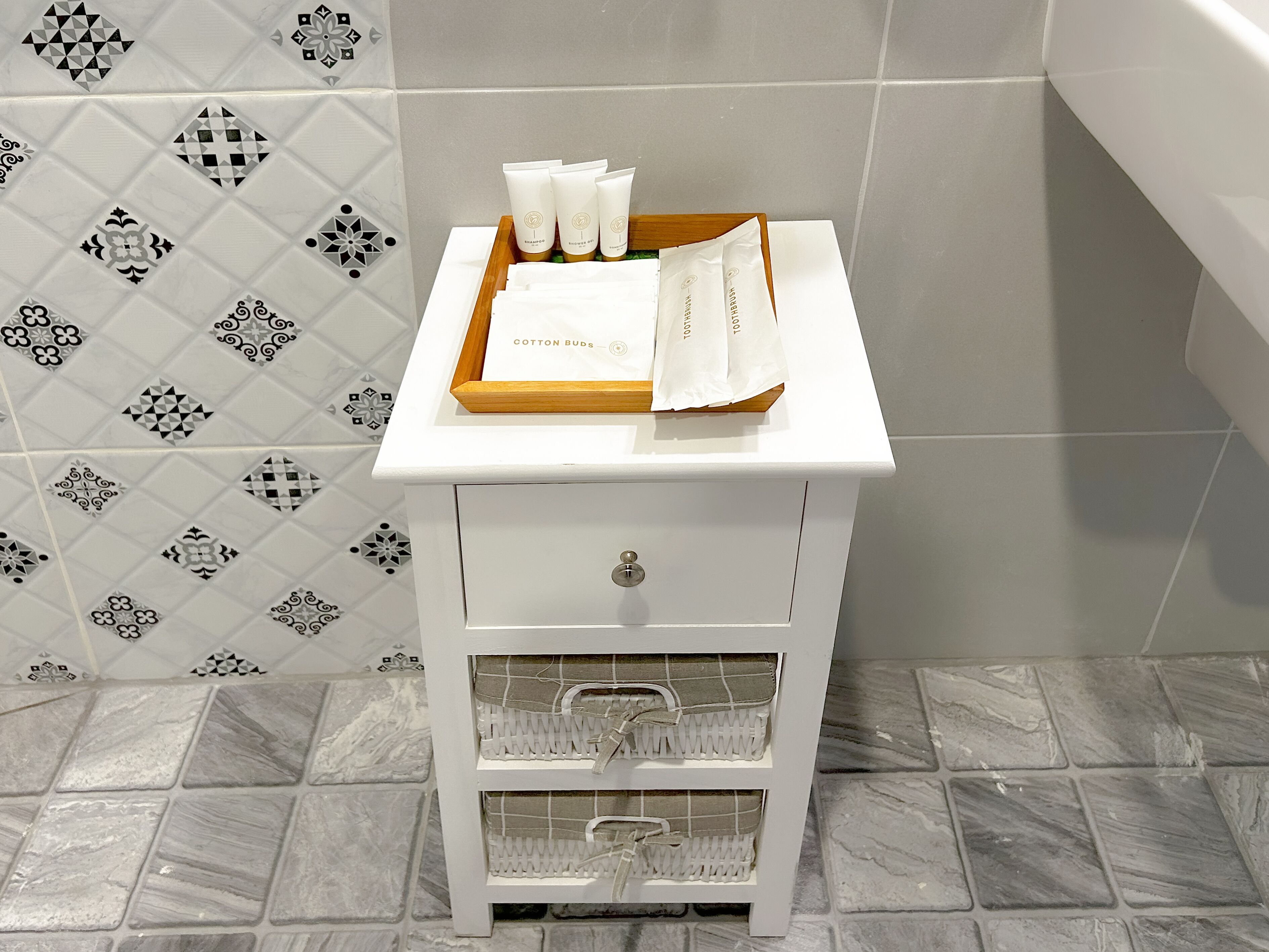 A bathroom vanity with a white cabinet, a tray with toiletries, and a patterned tile backsplash.