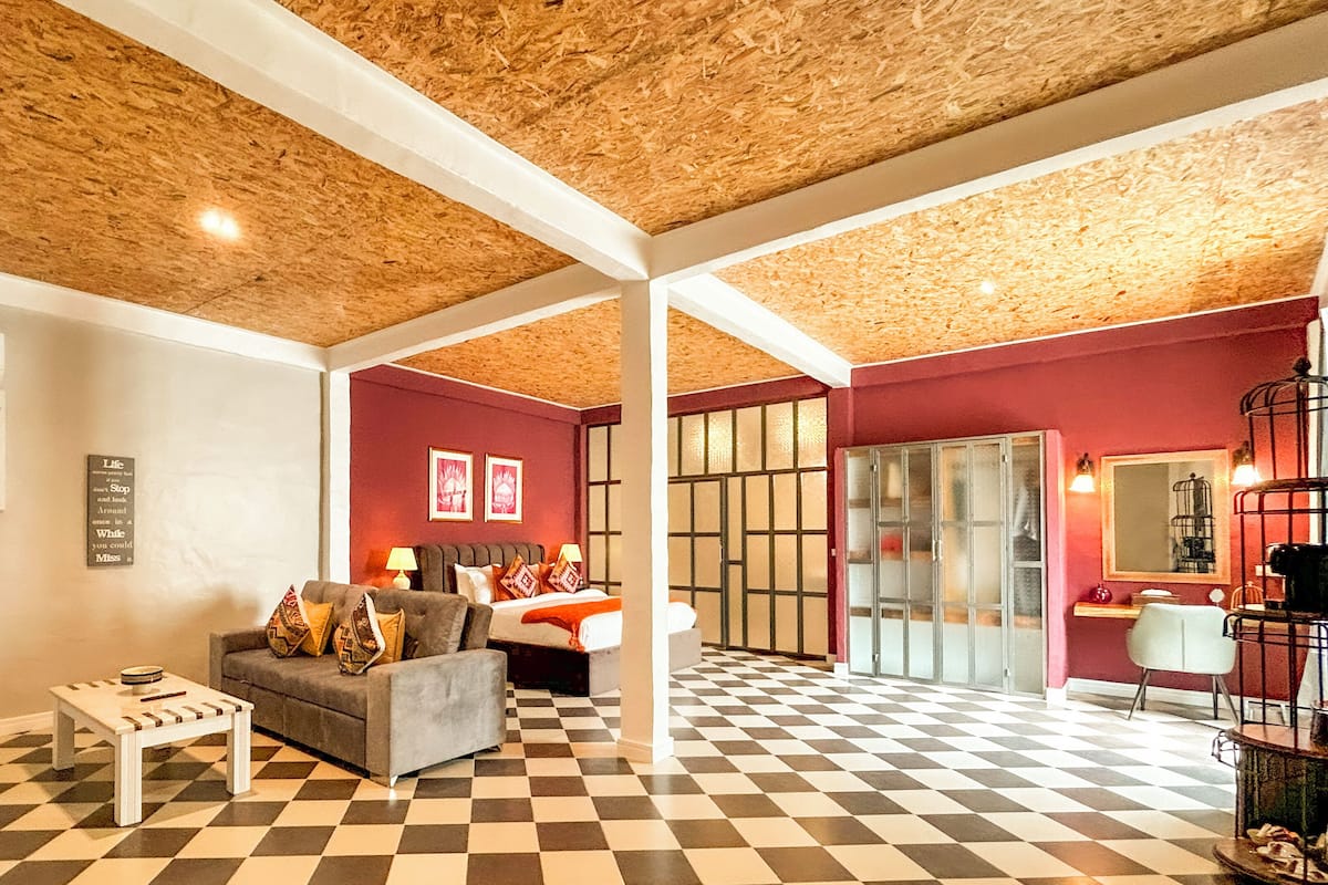 A hotel room with a checkered floor, a sofa, a bed, and a desk.
