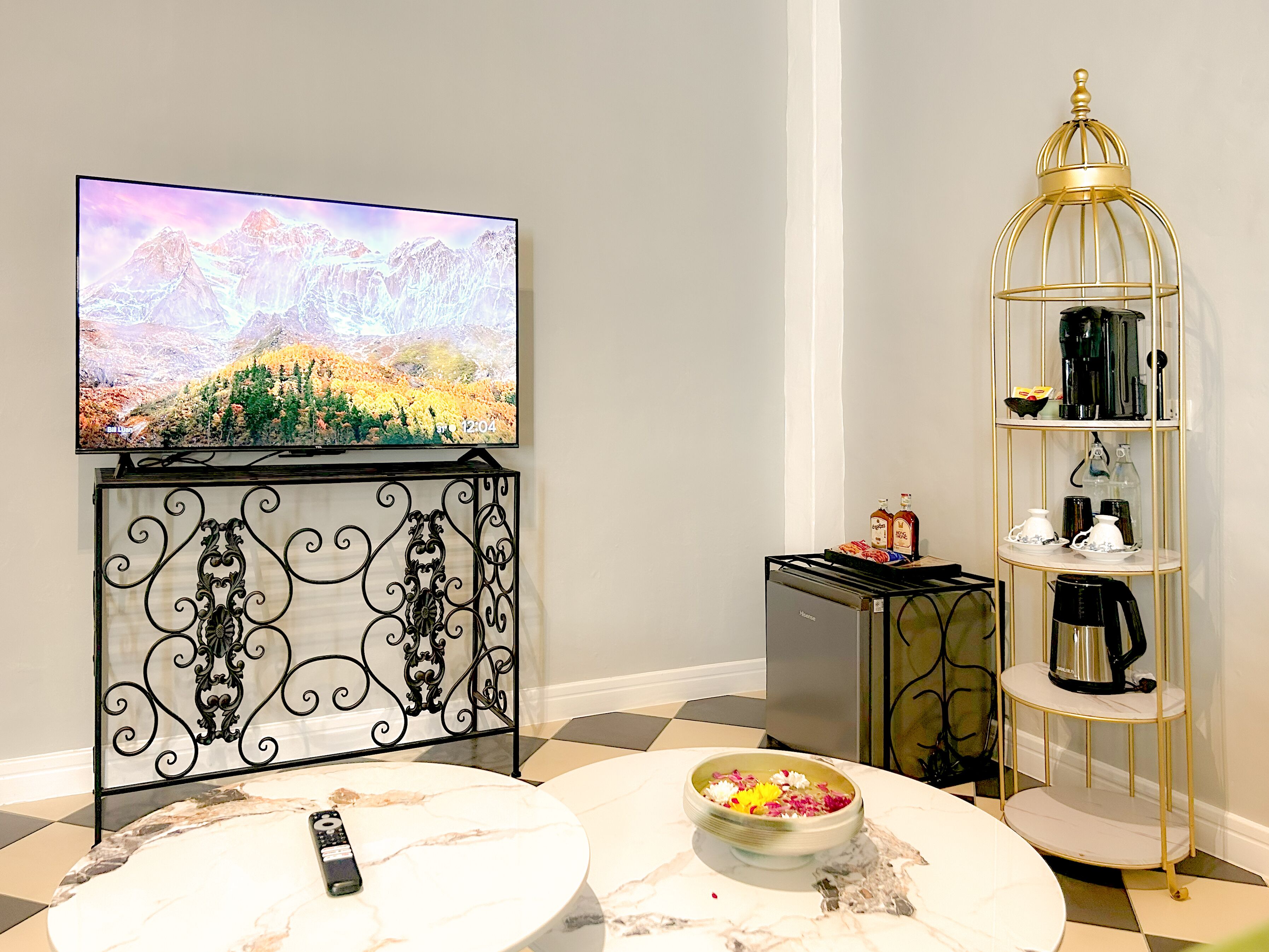 A living room with a TV, a coffee machine, a shelf with kitchenware, and a bowl of fruit on a marble table.