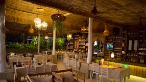 An outdoor dining area with thatched roof, white tables, and chairs, surrounded by greenery. - Milky Bay Resort (Ko Pha-ngan)