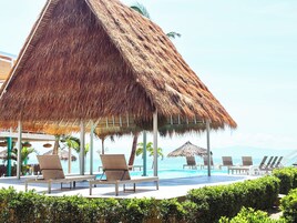 A beachside resort with a thatched-roof pavilion, lounge chairs, and a pool.
