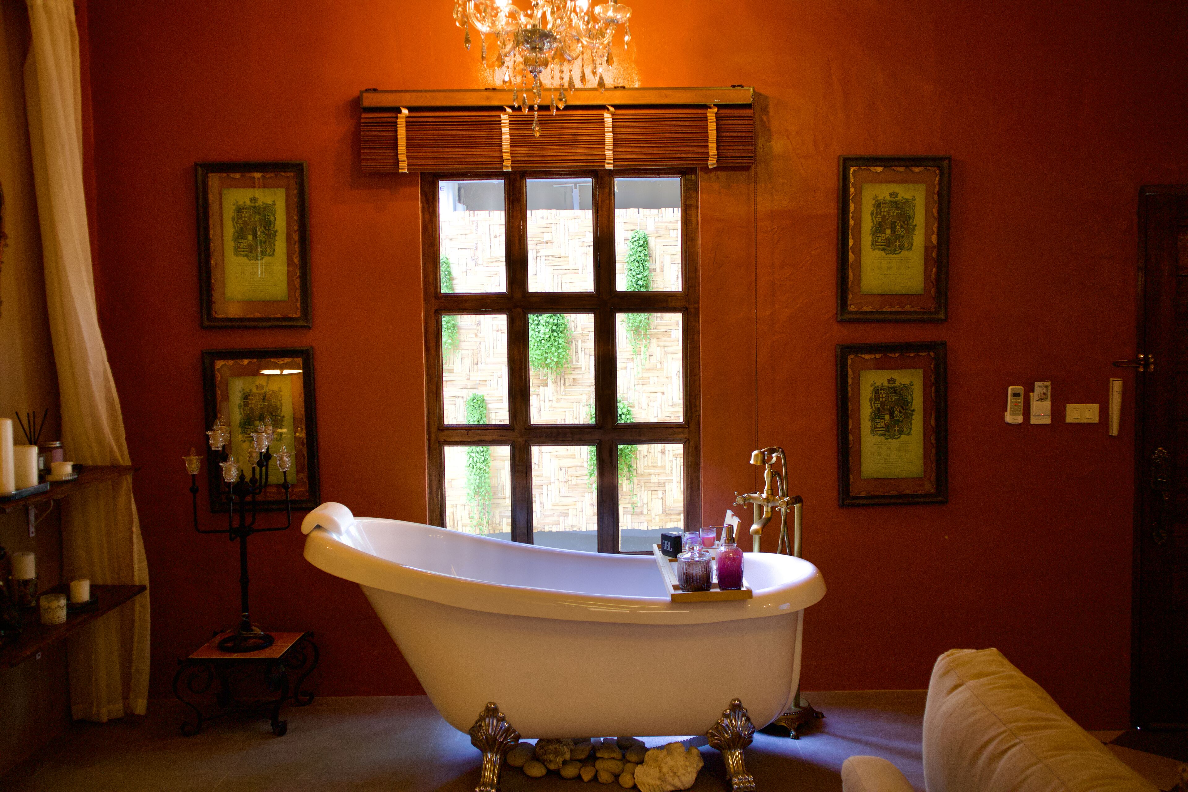 Une salle de bain avec une baignoire sur pieds, un lustre, des tableaux encadrés au mur et une fenêtre donnant sur un paysage verdoyant.