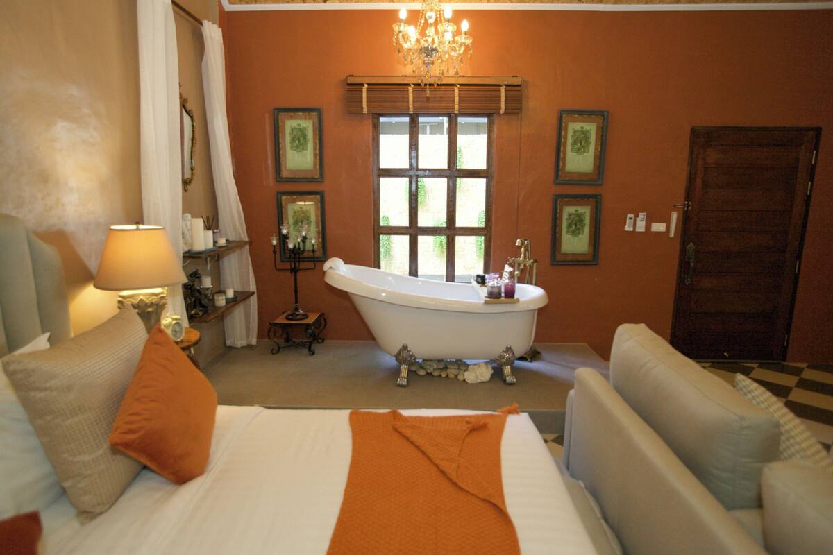 A bedroom with a large bed, a bathtub, and a chandelier.