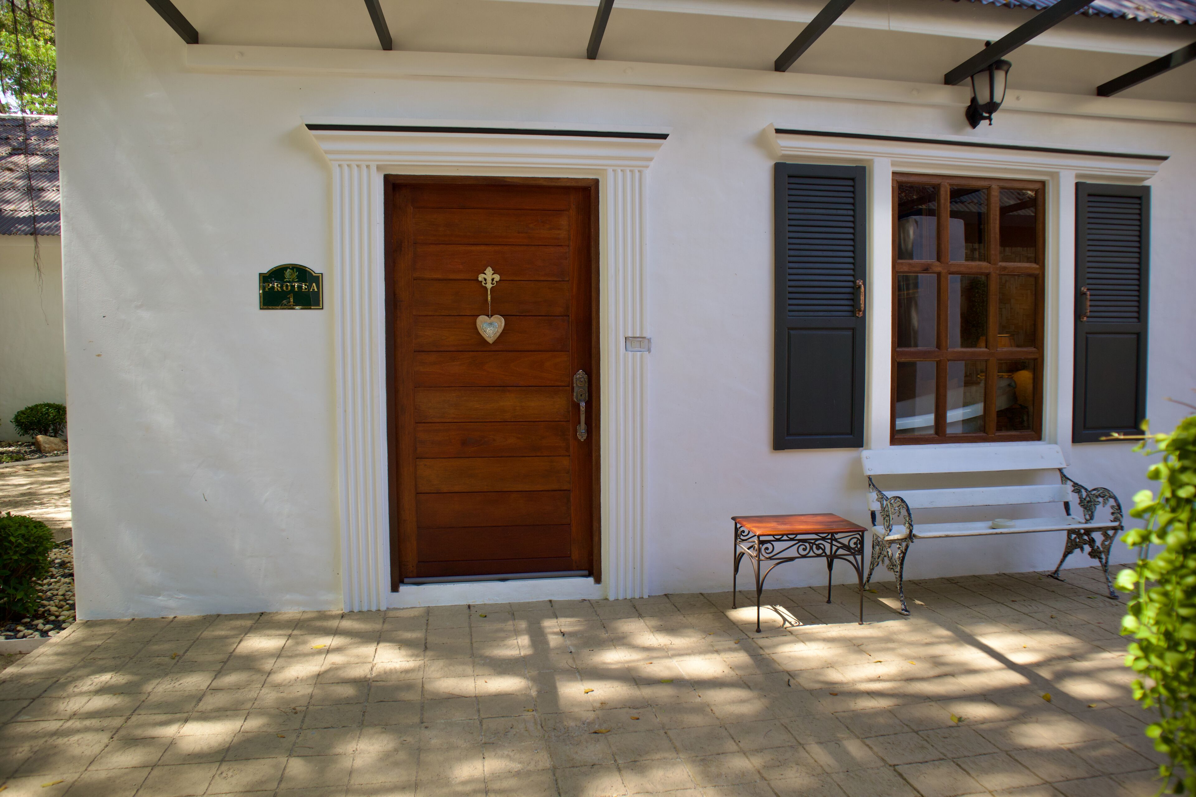 Um edifício branco com porta de madeira, um banco e uma pequena mesa na parte externa.