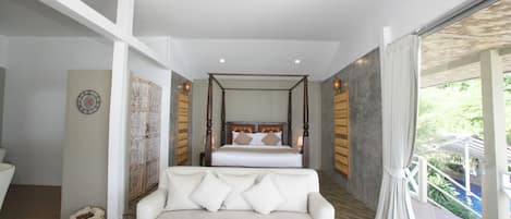 A bedroom with a four-poster bed, a white sofa, and a view of a pool.