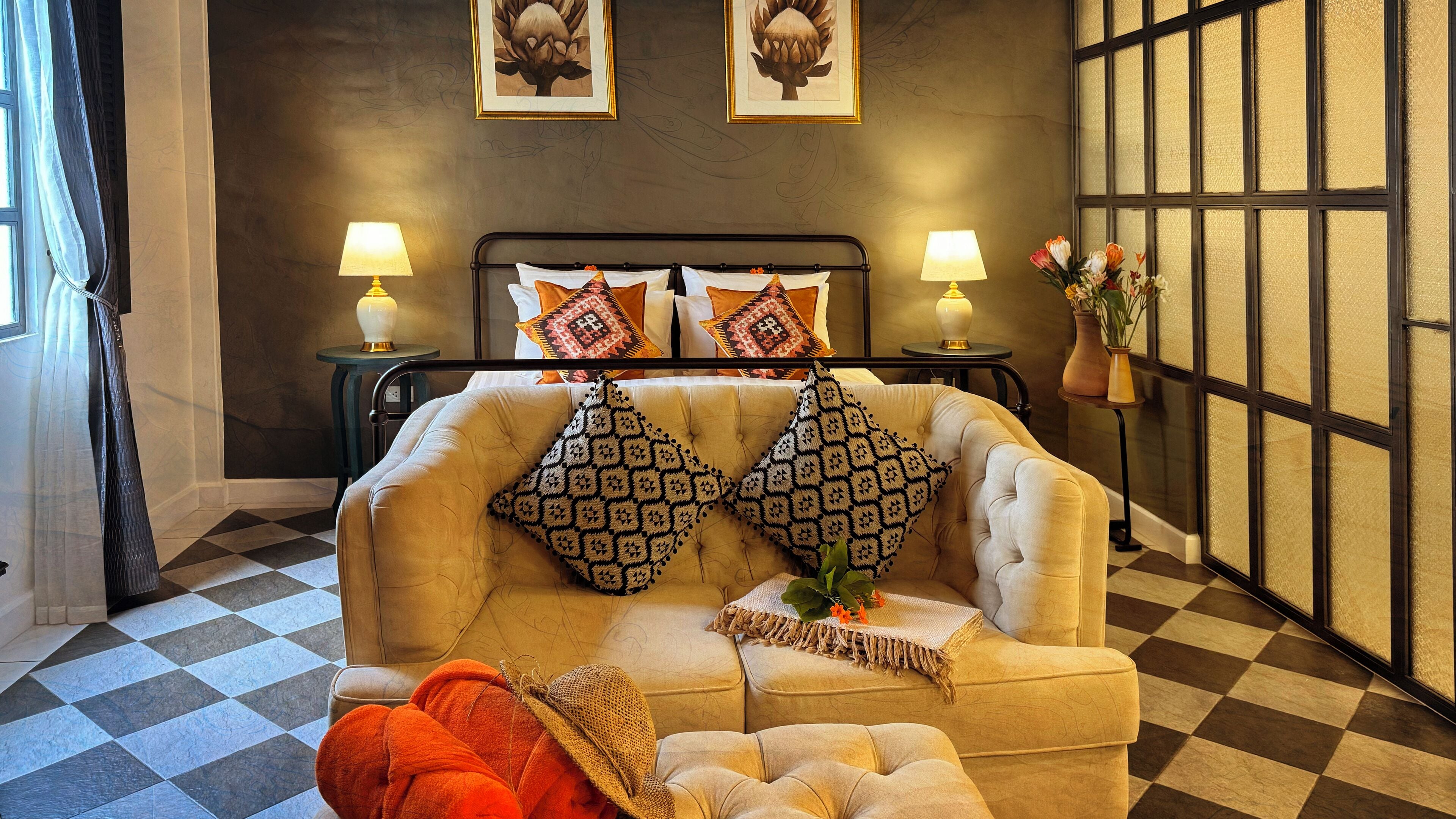 Una habitación con piso a cuadros, un sofá con cojines estampados, dos lámparas de noche y un jarrón con flores.