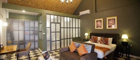Una habitación de hotel con piso a cuadros, un sofá, una cama con almohadas, una mesa, una silla y un candelabro.