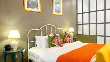 Een net opgemaakt bed met wit beddengoed en een oranje plaid, met aan beide kanten nachtkastjes en lampen, waarvan er één een Marshall speaker heeft.