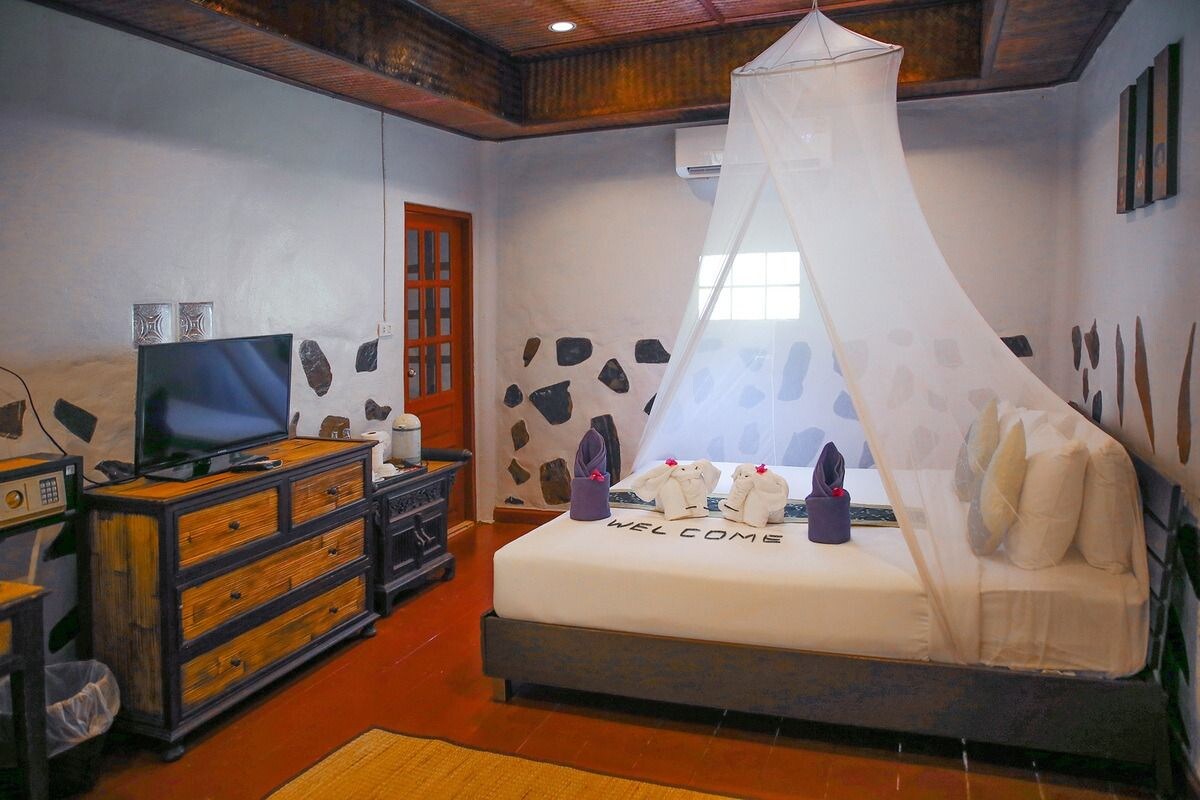 A bedroom with a bed, a television, a dresser, and a stone wall.