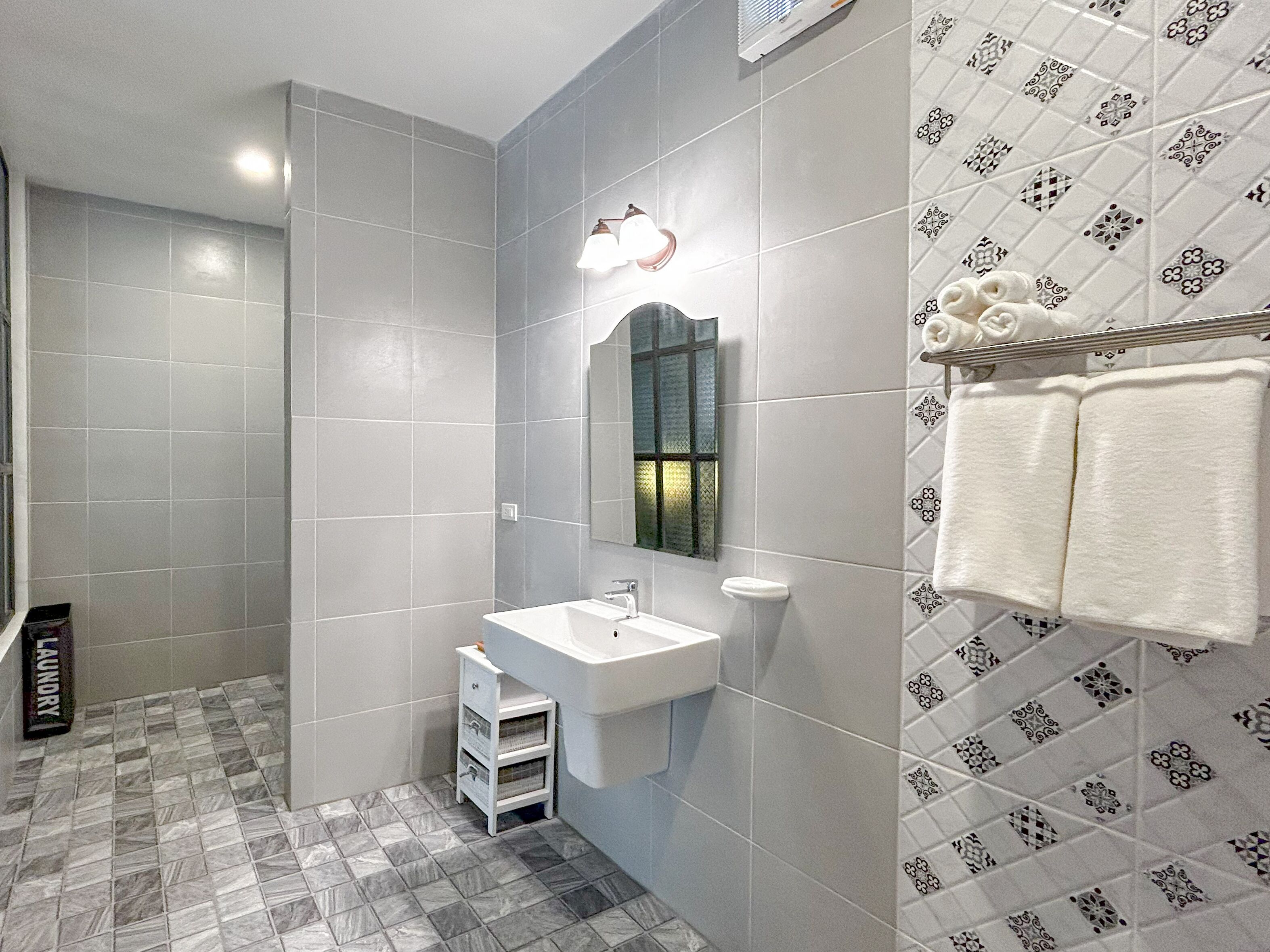 A bathroom with grey tiles, a white sink, a mirror, and a towel rack.