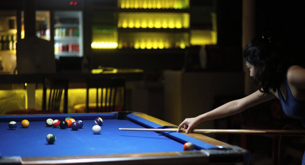 A pool table with balls and a cue stick, a bar area with bottles, and a sign for Milky Bay Resort.