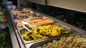 Un bufé con diversos platos, incluyendo macarrones, arroz amarillo y otros alimentos ya preparados.