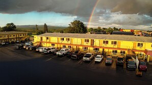 A motel with a parking lot full of cars, a visible rainbow, and a mountainous landscape in the background.