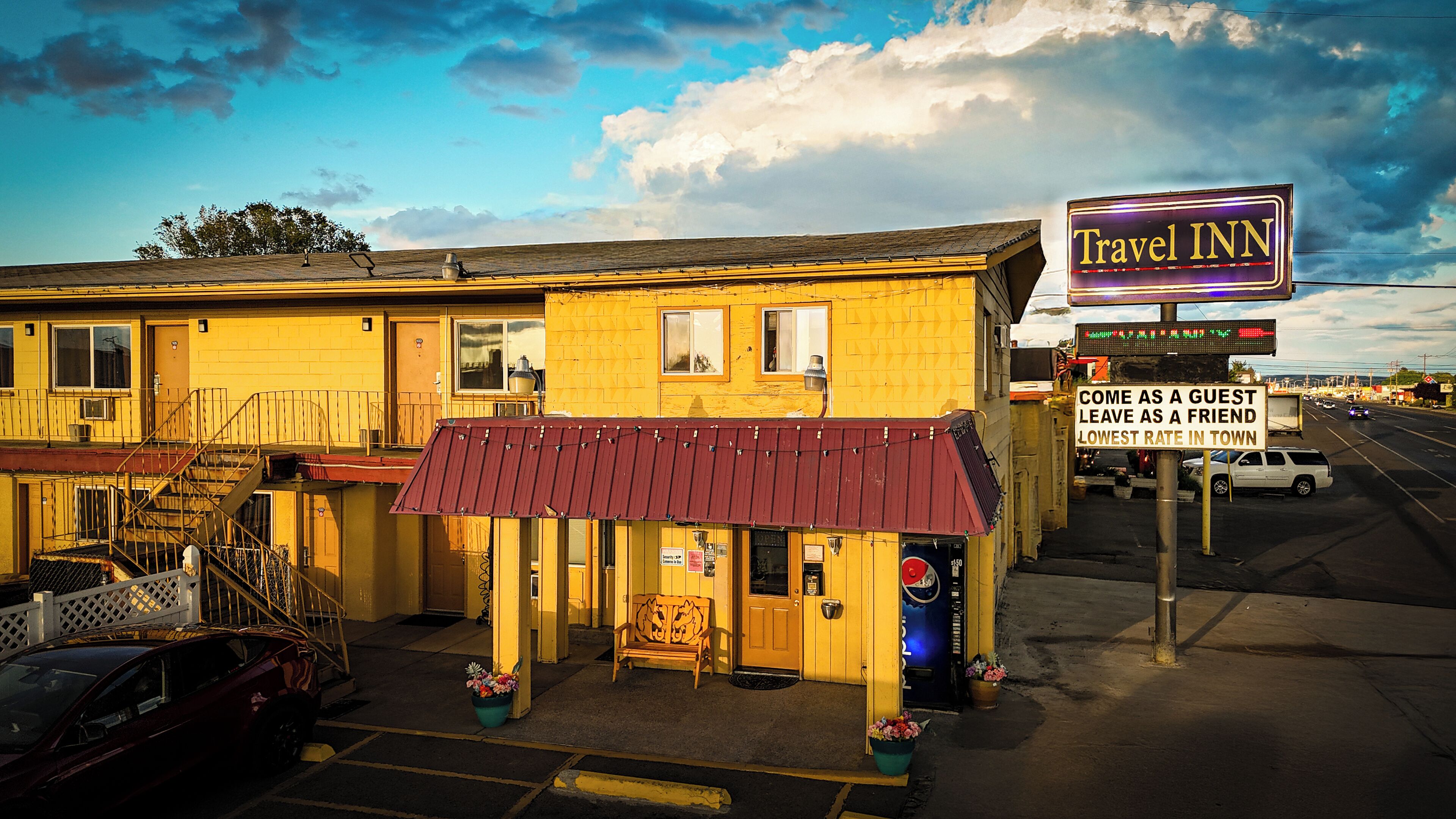 A Travel Inn with a red awning, a bench outside, and a sign advertising the lowest rate in town.