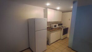 A compact kitchen with white cabinets, a refrigerator, a microwave, and a stove.