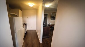 A narrow hallway with wooden flooring, white walls, and a kitchen area with white appliances.