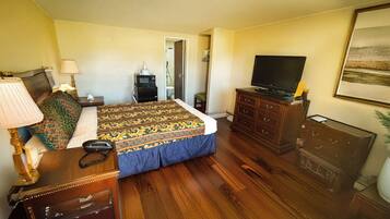 Une chambre d’hôtel avec un lit, un bureau, une commode, une télévision et une salle de bain visible à travers une porte ouverte.