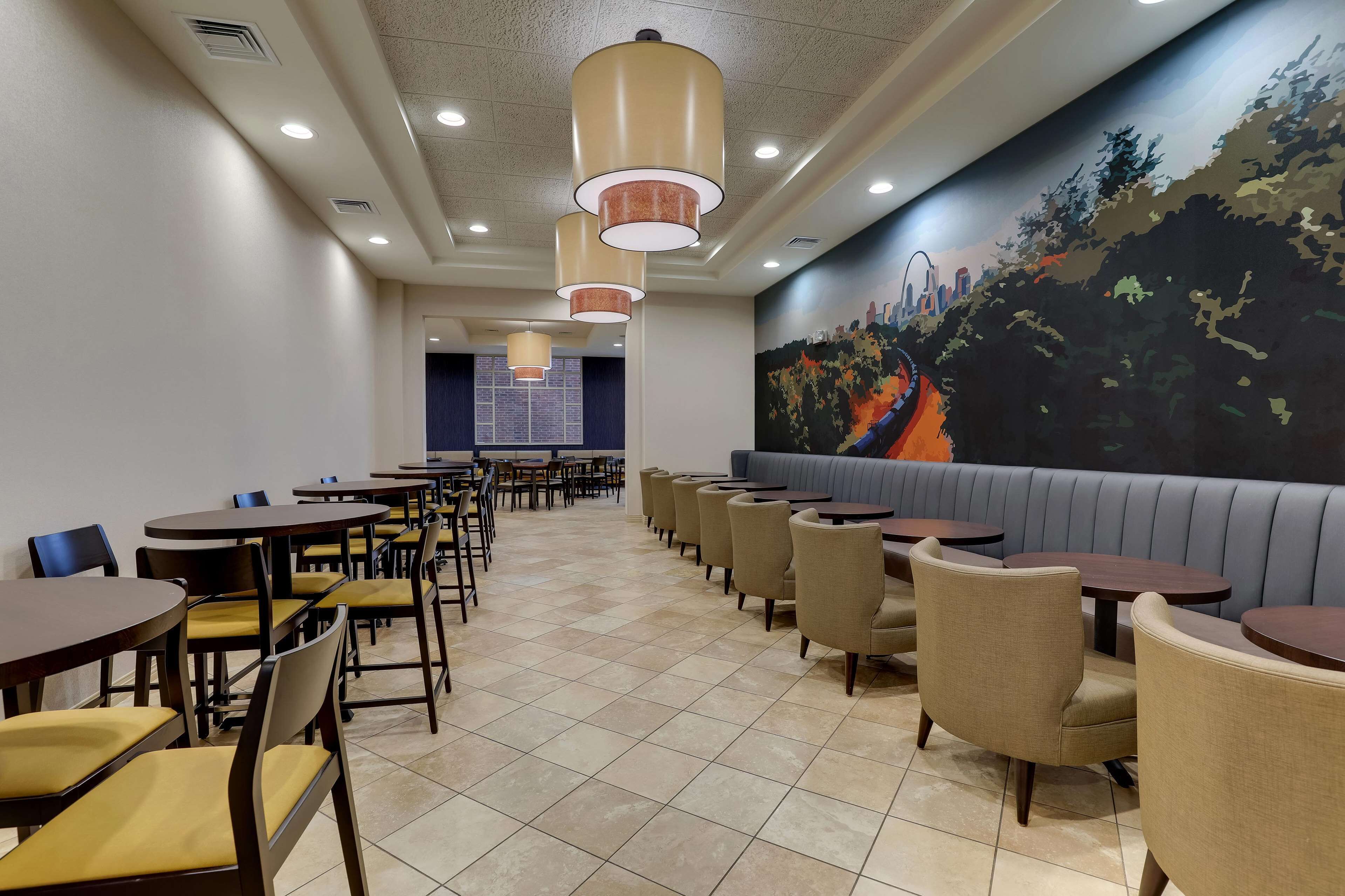 Un restaurante con varias mesas y sillas, un mural en la pared y luces empotradas en el techo.