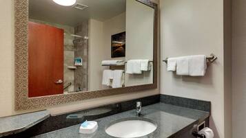 A bathroom with a large mirror, a sink, a towel rack, and a shower area.